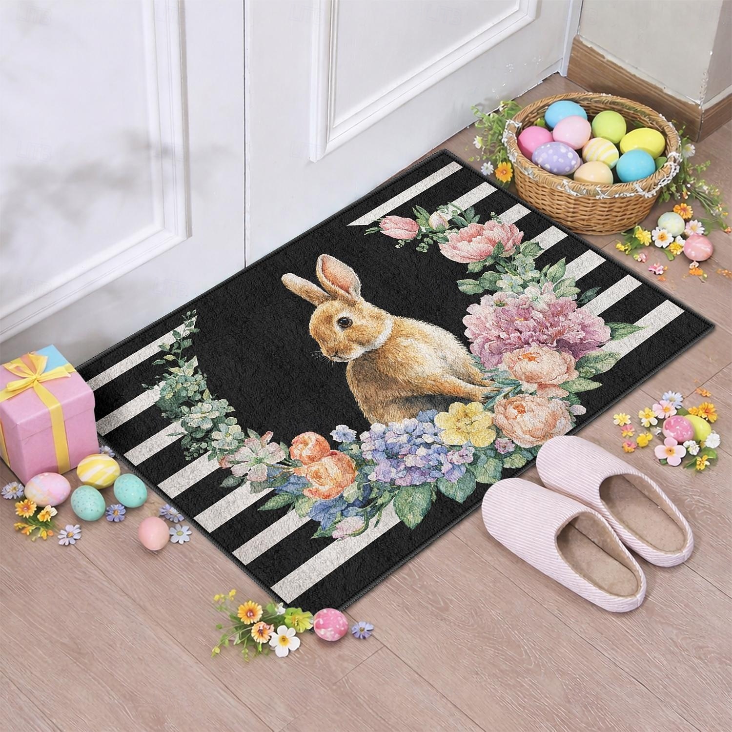 Felpudo de Pascua con forma de conejito rodeado de una corona floral floreciente sobre rayas blancas y negras, perfecto para dar la bienvenida a la primavera. 2026 - $16.99 –P1