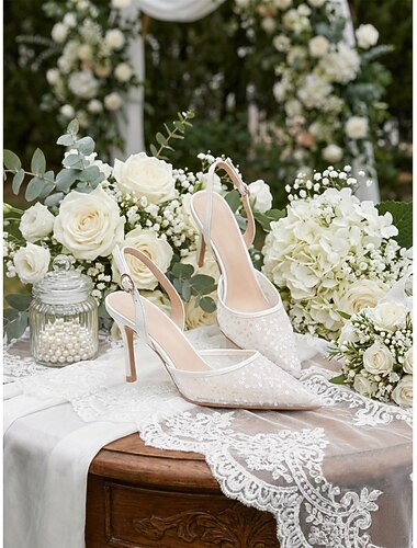  Sapato de salto alto feminino em renda marfim com bico fino e tira de pérolas no tornozelo, elegante para noivas em casamentos ao ar livre.